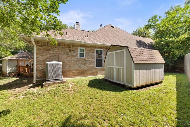 Back of house featuring central AC unit, a shed, an outdoor structure, a chimney, and brick siding | Image 39