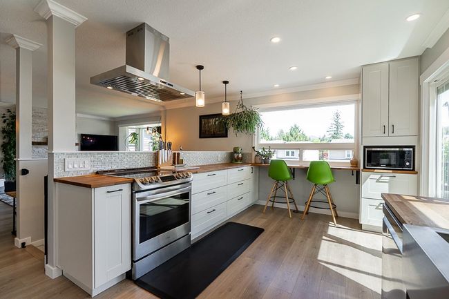 Kitchen with wood counters, wall chimney exhaust hood, stainless steel electric range, decorative backsplash, and ornamental molding | Image 11