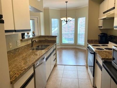 Bright, cozy kitchen featuring granite countertops, white cabinetry, modern appliances, and a charming dining nook with a bay window. | Image 3