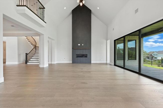 Unfurnished living room featuring high vaulted ceiling, light wood-style flooring, stairs, and a large fireplace | Image 12