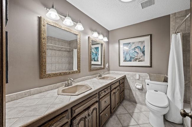 Main floor full bathroom with a double sink vanity, solid wood cabinets, easy to clean tile and a roof light tube added to offer natural light into the space | Image 34