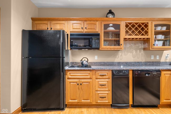 Bar kitchen with black appliances, light wood-style floors, stone countertops, and glass insert cabinets | Image 61