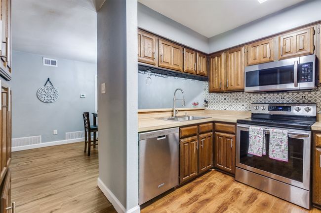 Kitchen with appliances with stainless steel finishes, light wood-style flooring, light countertops, tasteful backsplash, and brown cabinets | Image 10