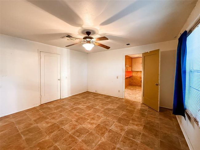 This primary bedroom features a ceiling fan with a light fixture, and double windows with blue curtains. | Image 10