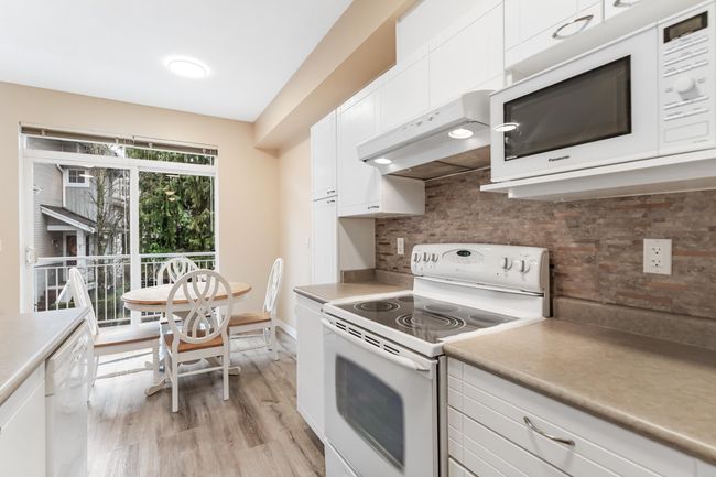 Kitchen featuring white appliances, tasteful backsplash, white cabinets, under cabinet range hood, and light countertops | Image 11