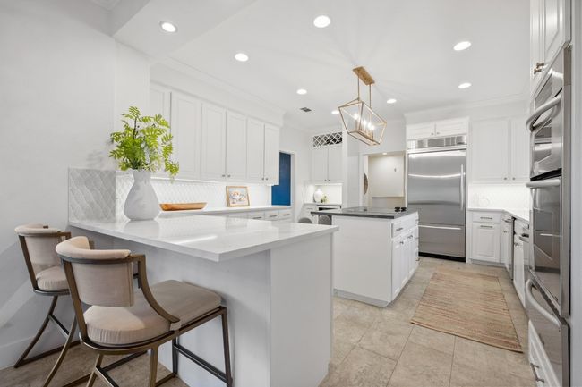 Kitchen with appliances with stainless steel finishes, tasteful backsplash, a peninsula, a kitchen island, and white cabinetry | Image 10