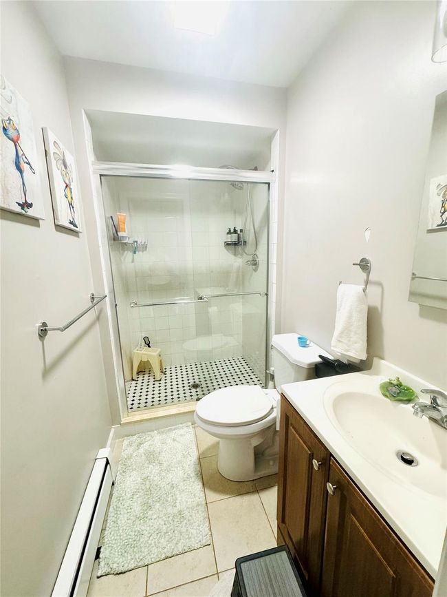 Bathroom featuring a baseboard heating unit, tile patterned floors, toilet, a shower stall, and vanity | Image 7