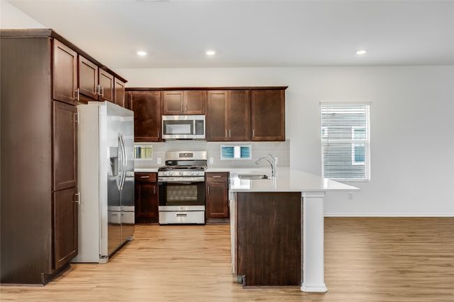 Kitchen featuring appliances with stainless steel finishes, a peninsula, light wood-type flooring, light countertops, and recessed lighting | Image 11