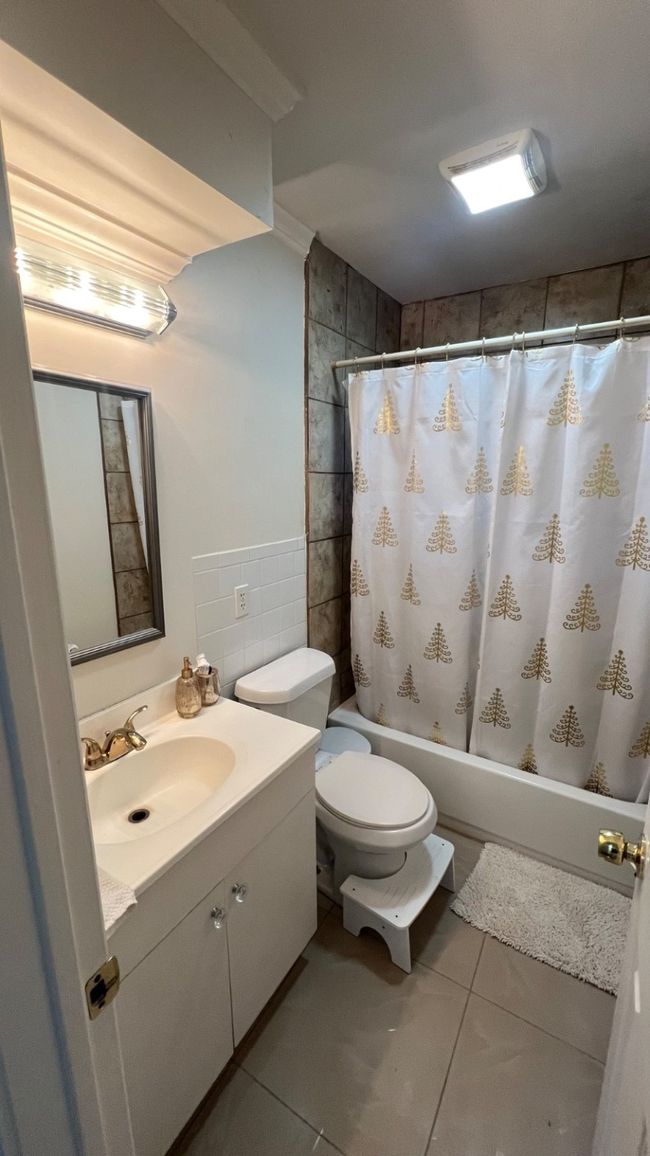 Bathroom with tile walls, vanity, shower / bath combination with curtain, toilet, and tile patterned flooring | Image 10