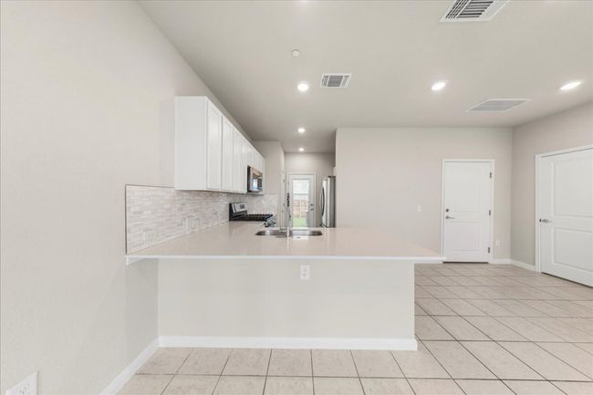Kitchen with stainless steel appliances, a peninsula, light countertops, a sink, and white cabinets | Image 10