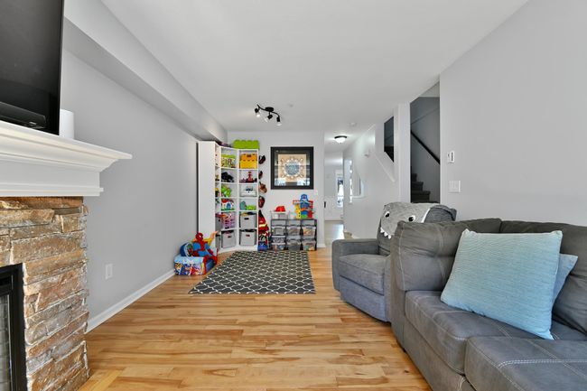 Living room with wood finished floors, a stone fireplace, and stairs | Image 5