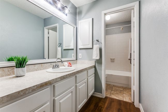 Bathroom featuring a textured ceiling, vanity, wood finished floors, tub / shower combination, and a textured wall | Image 23