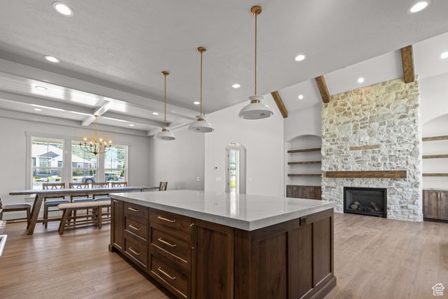 Kitchen featuring beamed ceiling, light wood-type flooring, a stone fireplace, a center island, and a chandelier | Image 6