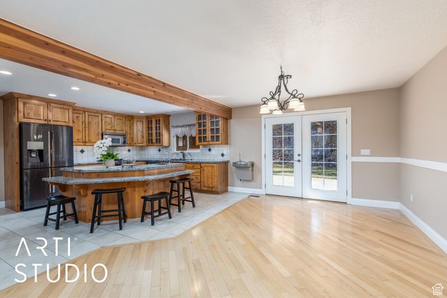 Kitchen with stainless steel microwave, a kitchen island, brown cabinets, a kitchen bar, and refrigerator with ice dispenser | Image 18