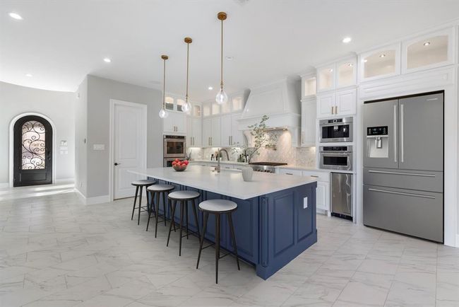 This stunning, fully remodeled kitchen dazzles with its spacious island, custom cabinetry with showcase uppers, and professional-grade appliances—all illuminated by elegant pendant lights and grounded in sleek marble-look tile. *This photo has been virtually staged.* | Image 7