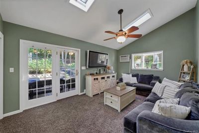 Living room featuring vaulted ceiling with skylight, carpet floors, a healthy amount of sunlight, and an AC wall unit | Image 3