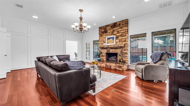 Living area with a decorative wall, a chandelier, wood finished floors, a stone fireplace, and recessed lighting | Image 16