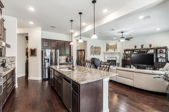 Kitchen featuring dark brown cabinetry, a fireplace, stainless steel appliances, dark wood-style floors, and light stone counters | Image 5