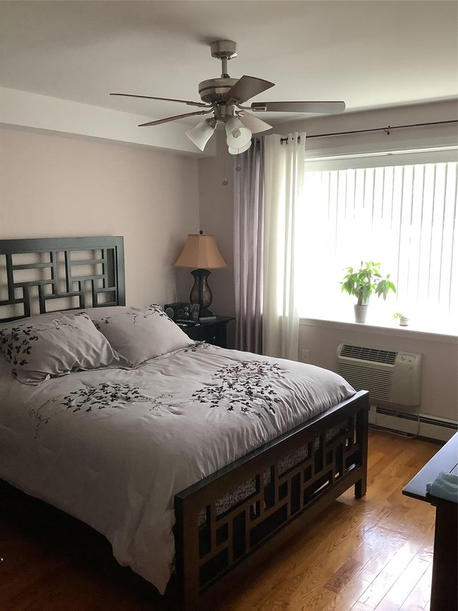 Bedroom featuring a wall mounted AC, a baseboard radiator, wood finished floors, and ceiling fan | Image 5