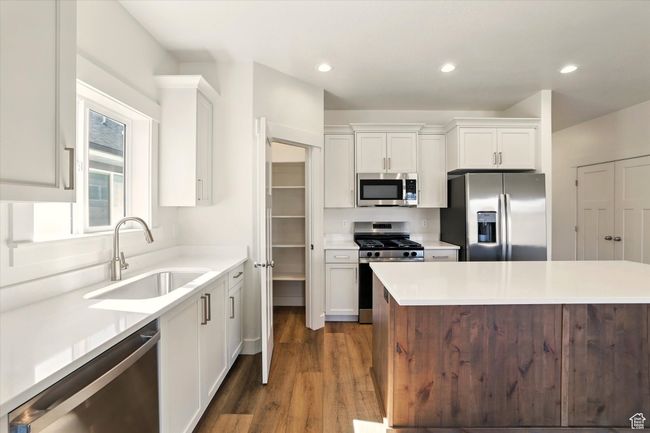 Kitchen featuring stainless steel appliances, a sink, white cabinetry, dark wood finished floors, and light countertops | Image 14