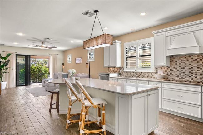 Kitchen featuring custom exhaust hood, a center island, a breakfast bar, hanging light fixtures, and black stovetop | Image 13