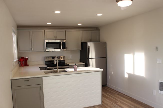 Kitchen with gray cabinetry, appliances with stainless steel finishes, a peninsula, light wood finished floors, and light countertops | Image 7