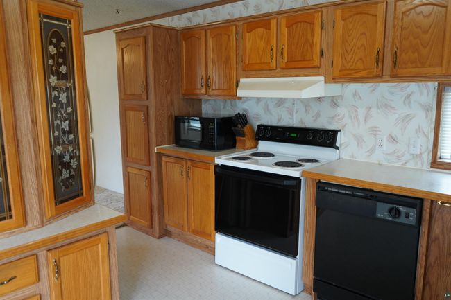Kitchen with black appliances, light countertops, brown cabinetry, premium range hood, and crown molding | Image 11