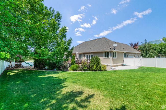 Back of house with a fenced backyard, a patio area, a playground, stucco siding, and a gate | Image 43