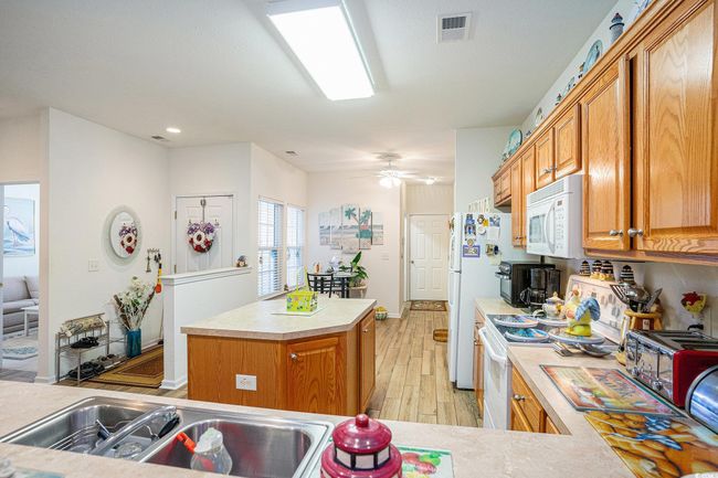 Kitchen with white appliances, light countertops, light wood-type flooring, a kitchen island, and recessed lighting | Image 6