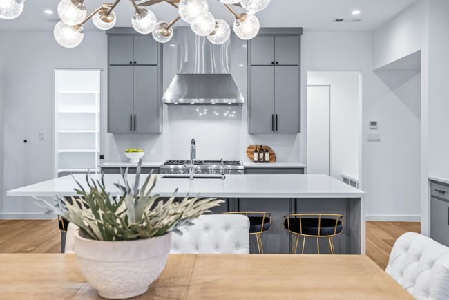 Kitchen featuring gray cabinets, wall chimney exhaust hood, a chandelier, light wood-style floors, and light countertops | Image 11
