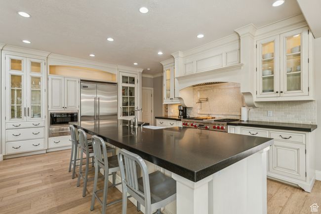 Kitchen with dark countertops, built in appliances, light wood-style flooring, decorative backsplash, and ornamental molding | Image 17