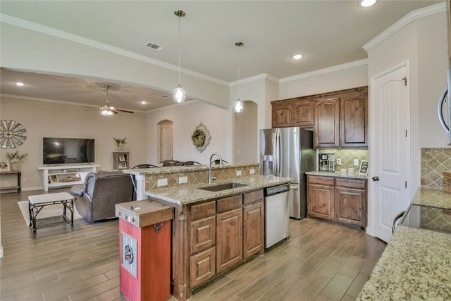 Kitchen with arched walkways, wood finished floors, a sink, stainless steel appliances, and a center island with sink | Image 11