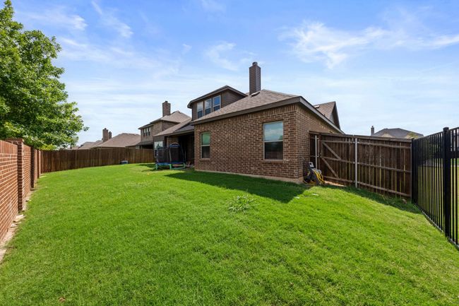 Back of property featuring a trampoline, brick siding, a fenced backyard, a shingled roof, and a chimney | Image 23