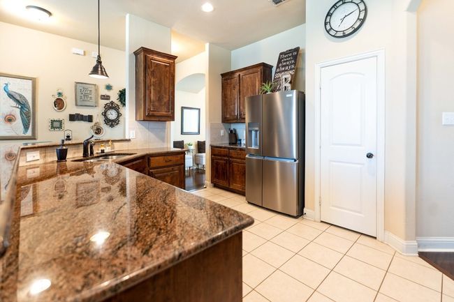 Kitchen with stainless steel fridge, dark stone counters, light tile patterned floors, a peninsula, and pendant lighting | Image 13