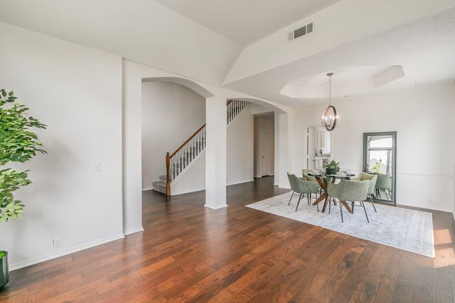Dining space featuring a tray ceiling, arched walkways, dark wood-style flooring, visible vents, and stairs | Image 8