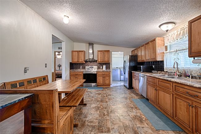 Kitchen with brown cabinetry, tasteful backsplash, stainless steel appliances, stone finish floors, and a textured ceiling | Image 6
