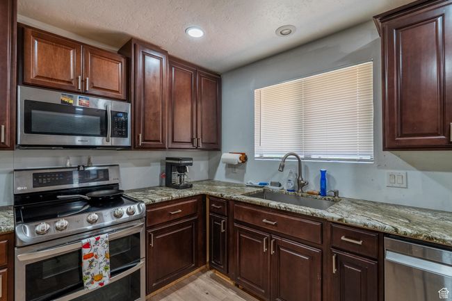 Kitchen with appliances with stainless steel finishes, light stone countertops, light wood-style floors, a textured ceiling, and recessed lighting | Image 25