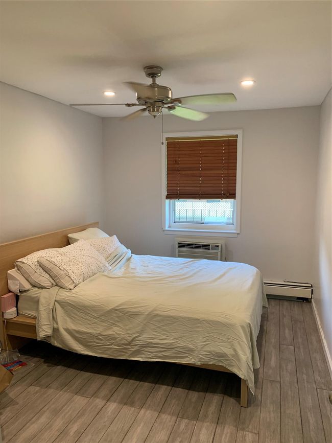 Bedroom with wood finished floors, an AC wall unit, a baseboard heating unit, a ceiling fan, and recessed lighting | Image 5