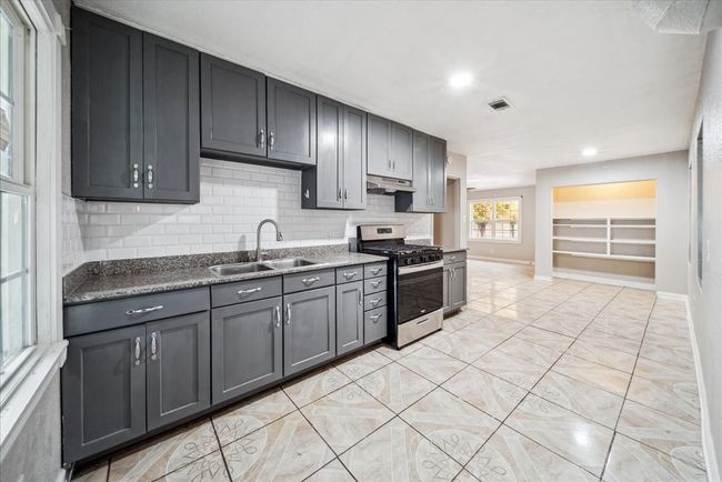 Kitchen with stainless steel gas stove, under cabinet range hood, gray cabinets, tasteful backsplash, and recessed lighting | Image 9