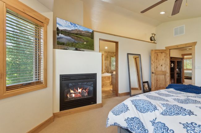 Carpeted bedroom featuring baseboards, vaulted ceiling, multiple windows, connected bathroom, and a glass covered fireplace | Image 27