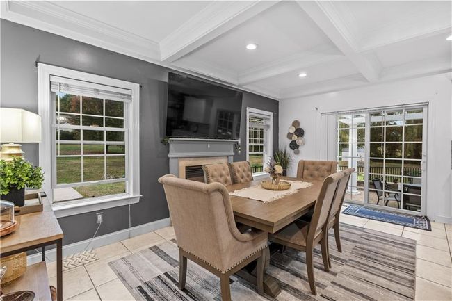 Dining room featuring light tile patterned floors, beam ceiling, coffered ceiling, a fireplace, and baseboards | Image 11