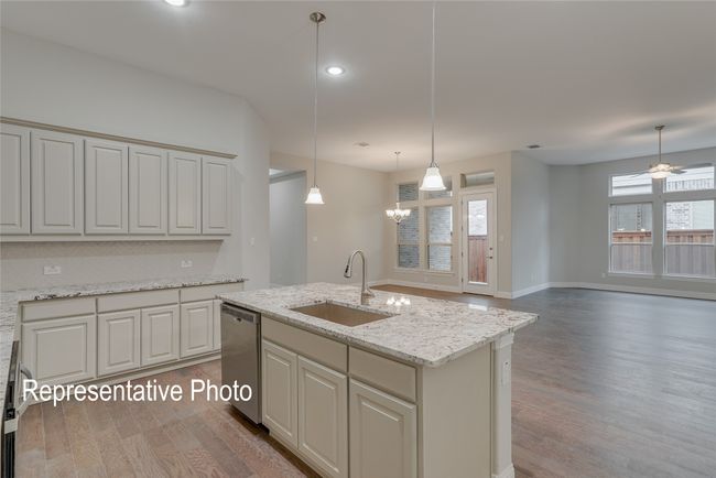 Kitchen with stainless steel dishwasher, light wood-type flooring, decorative light fixtures, a kitchen island with sink, and light stone countertops | Image 5
