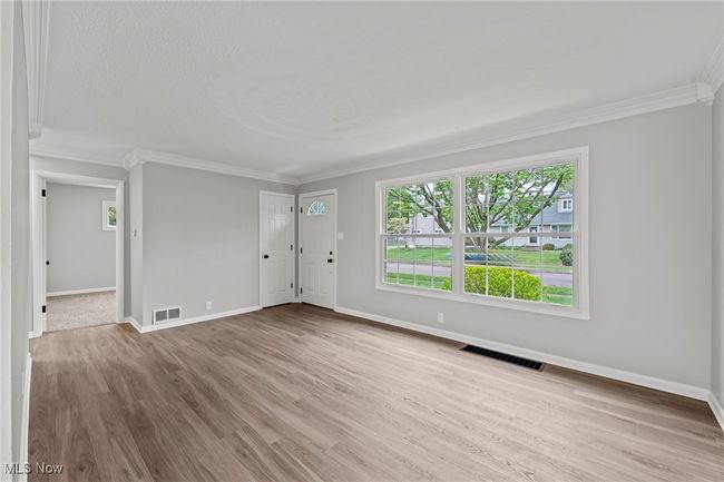 Unfurnished living room featuring a wealth of natural light, visible vents, ornamental molding, and baseboards | Image 8