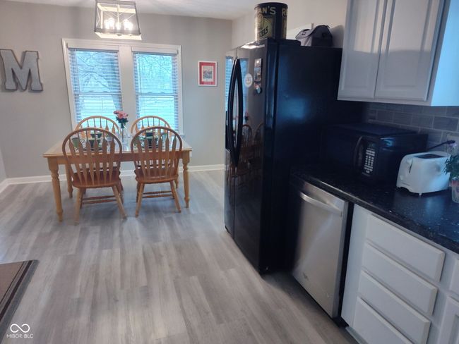 kitchen with a notable chandelier, dark countertops, light wood-style floors, black microwave, and dishwasher | Image 8