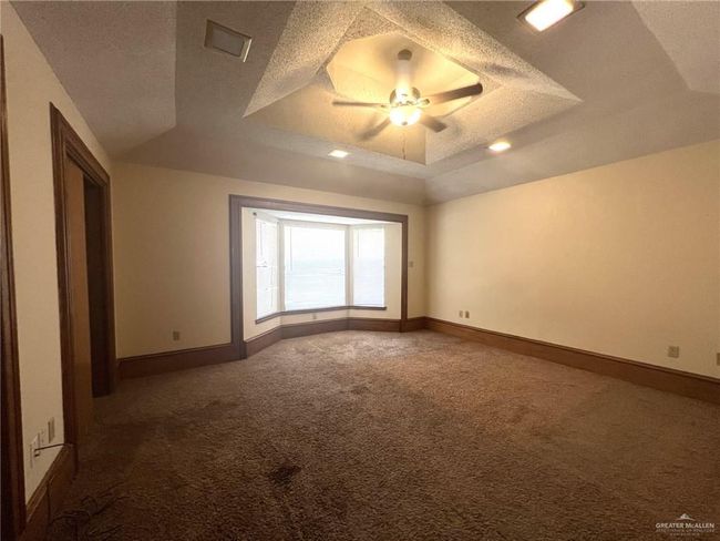 Empty room with a textured ceiling, carpet, a tray ceiling, and ceiling fan | Image 9