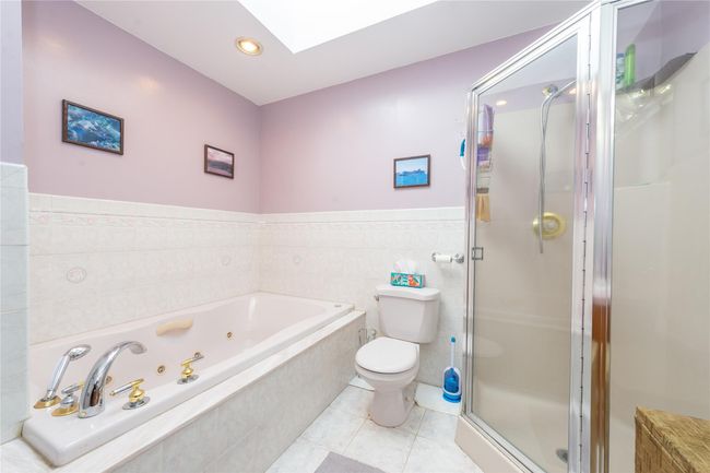 Bathroom with a skylight, tile walls, toilet, a shower stall, and tile patterned floors | Image 29