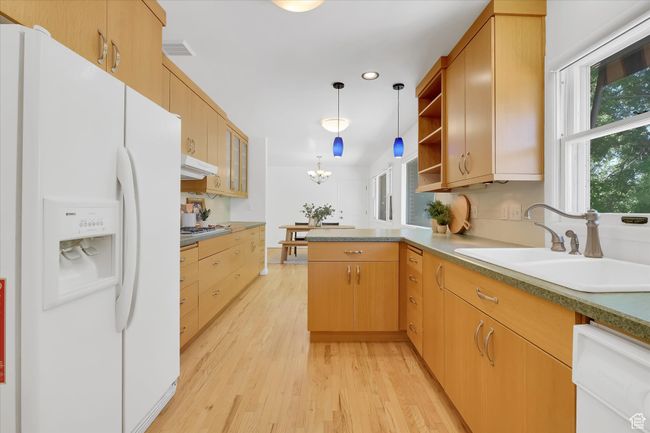 Kitchen featuring white fridge with ice dispenser, dishwasher, a peninsula, light wood finished floors, and under cabinet range hood | Image 9