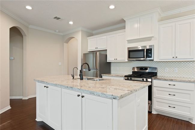 Kitchen featuring appliances with stainless steel finishes, a kitchen island with sink, white cabinets, tasteful backsplash, and crown molding | Image 4