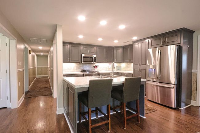 Kitchen featuring stainless steel appliances, light countertops, dark wood-style floors, decorative backsplash, and an island with sink | Image 6