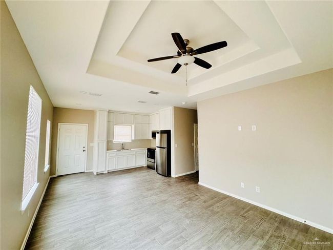 Unfurnished living room with a tray ceiling, a ceiling fan, light wood finished floors, and plenty of natural light | Image 14